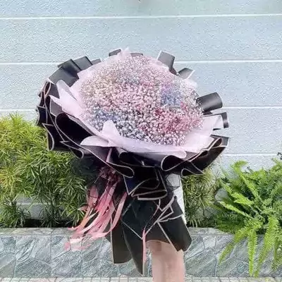A person holds a large bouquet of rainbow-colored baby's breath flowers wrapped in black and pink paper.