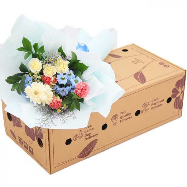 Bouquet of white, yellow, pink, and blue flowers in a cardboard box.