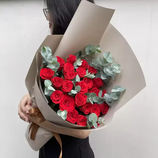 A bouquet of red roses and eucalyptus, wrapped in brown paper with a ribbon.