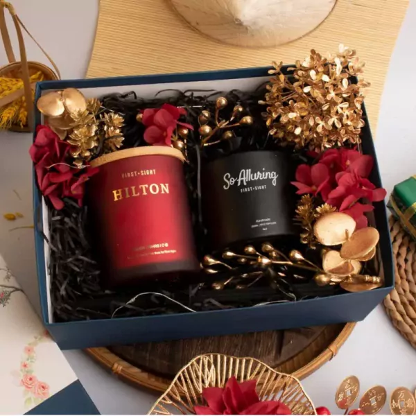 Gift box with red and black scented candles, gold and red floral decorations, and shredded paper filler.