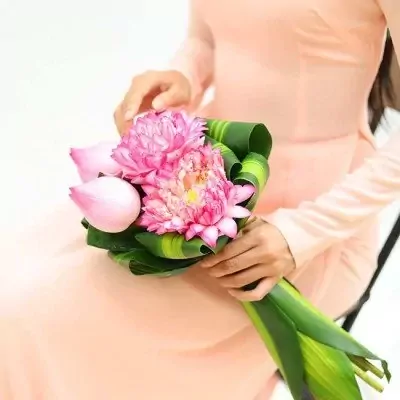 Pink lotus bouquet with green leaves held by a person in a peach dress.