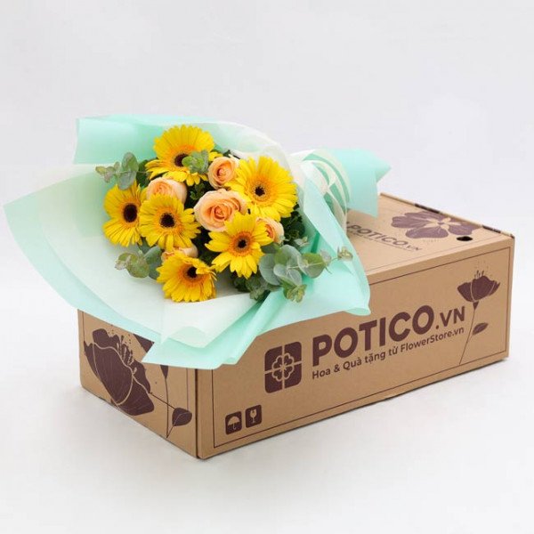 Sunshine Bouquet with yellow gerberas and peach roses in light blue wrapping, on a cardboard box.