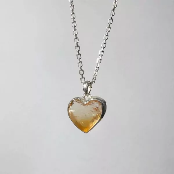 Silver chain necklace with a heart-shaped, raw yellow crystal pendant.