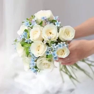 White roses and blue flowers in a bridal bouquet held by hands.