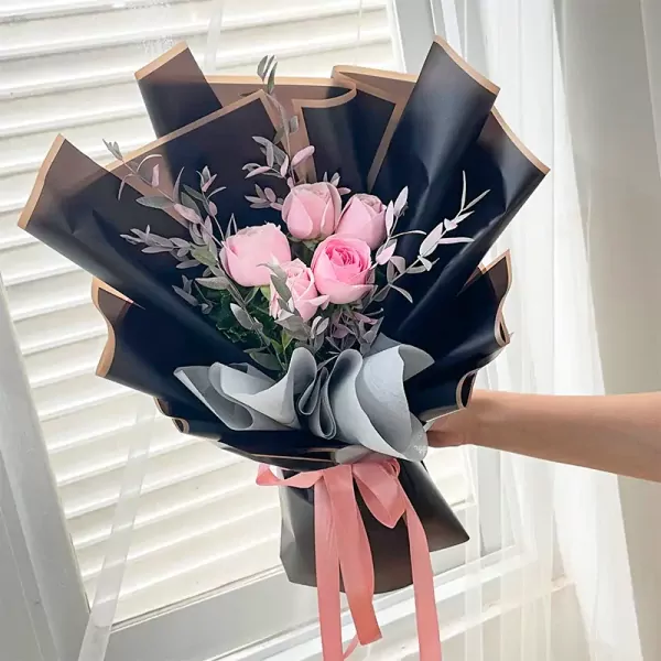 Pink roses and eucalyptus bouquet wrapped in black and brown paper, tied with a pink ribbon.