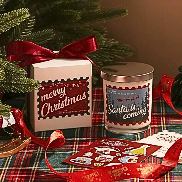 Christmas gift set: candle and box with festive designs, red ribbon, and pine branches.