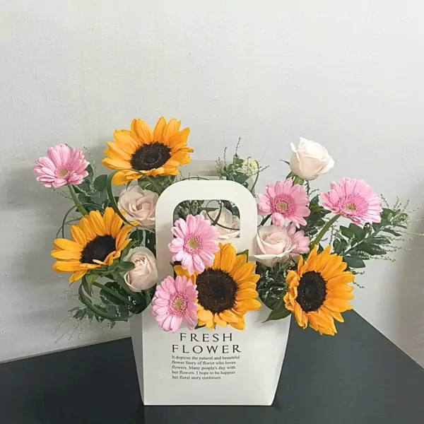 Floral arrangement in a white box with sunflowers, pink gerbera daisies, and white roses.