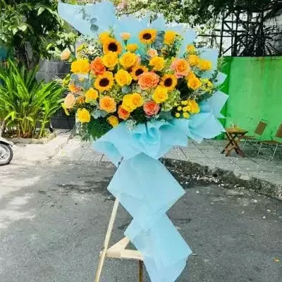 Large bouquet of yellow and orange roses, sunflowers, and hydrangeas on a stand.