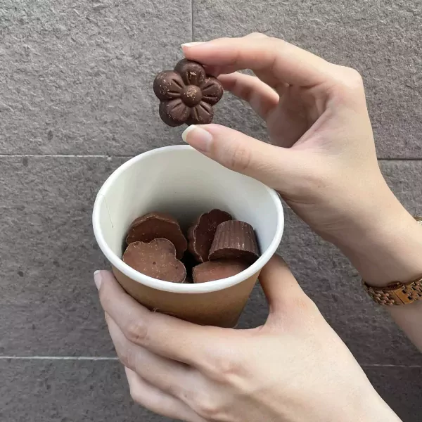 Hand holding a flower-shaped chocolate above a cup of chocolates.