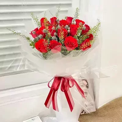 Bouquet of 18 red roses with decorative foliage, wrapped in clear cellophane and tied with a red ribbon.
