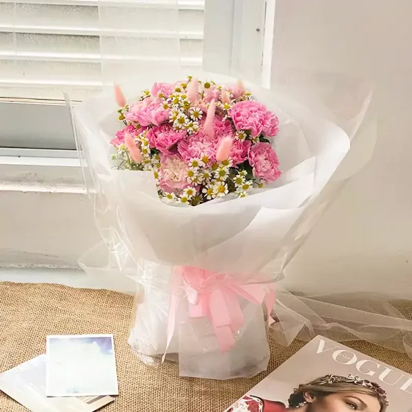 Pink carnation and daisy bouquet with fluffy pink accents, wrapped in white paper and tied with a pink ribbon.