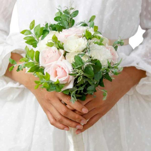 Bride holding a bouquet of pink and white roses with greenery.