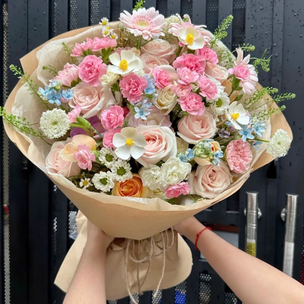Pink and white flowers including roses, gerbera daisies, and carnations wrapped in brown paper.
