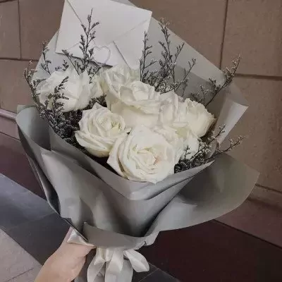 Bouquet of white roses wrapped in grey paper with a white envelope and ribbon.