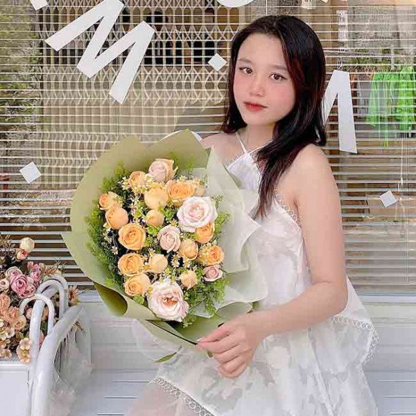 Woman holding a bouquet of cream and yellow roses with daisies.