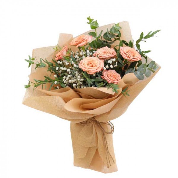Peach roses, baby's breath, and eucalyptus in brown paper wrapping, tied with twine.