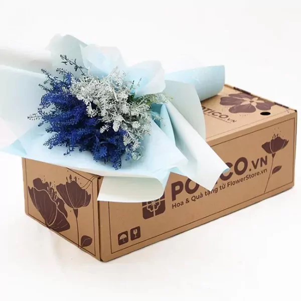 A bouquet of blue and silver dried flowers rests on a cardboard box with floral designs.
