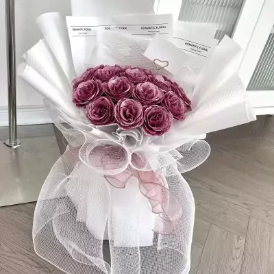 A bouquet of deep pink roses wrapped in white paper and tulle.