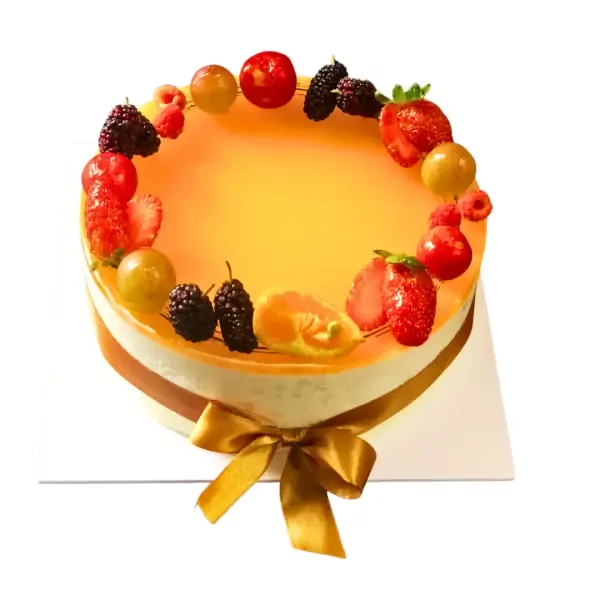 Round, orange mousse cake with fresh berries and fruits on top, tied with a golden bow.