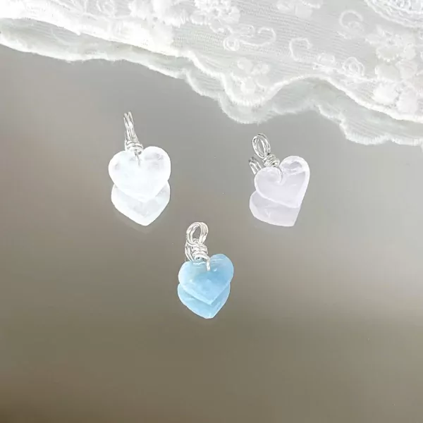 Three heart-shaped stone pendants, clear quartz, rose quartz, and aquamarine, on a mirrored surface.