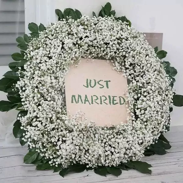 Wedding car wreath with "Just Married" banner, made of baby's breath and greenery.