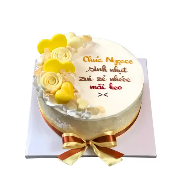 A white cake with yellow and white frosting flowers and hearts, and a yellow and brown ribbon bow.