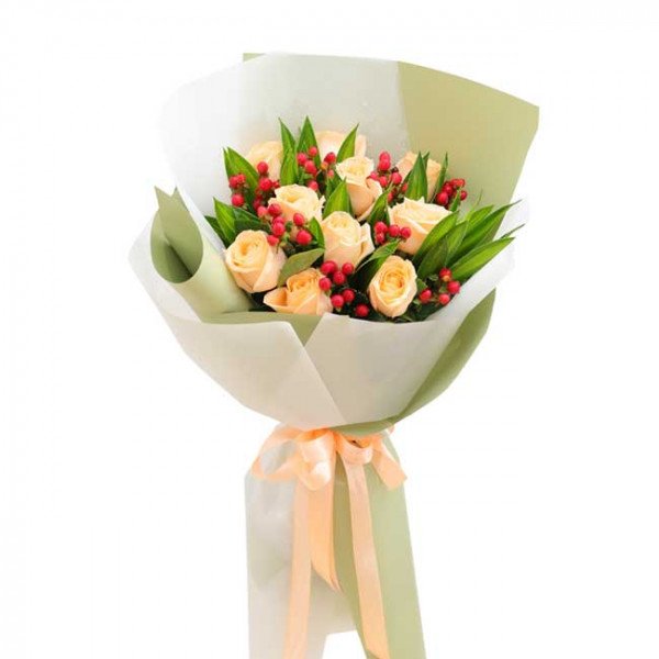 Peach roses and red berries in a bouquet with light green and white wrapping, tied with a peach ribbon.