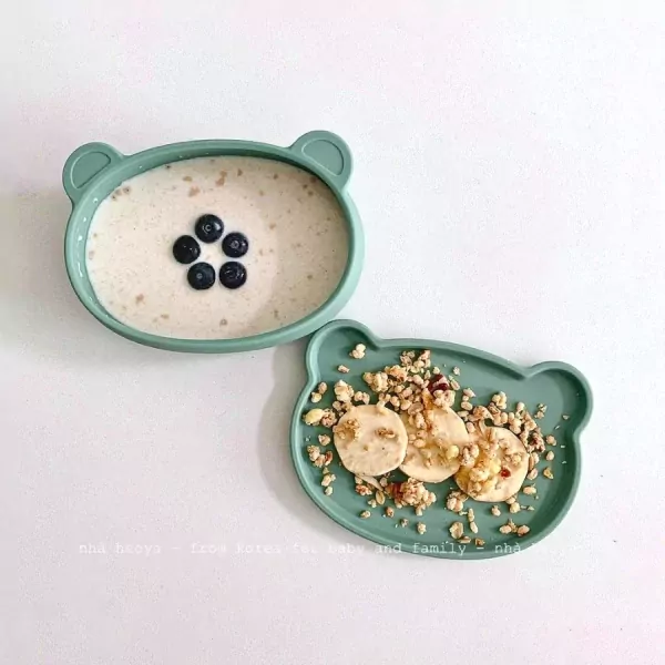 Cute bear-shaped silicone bowls with oatmeal and blueberries, and a plate with banana slices and granola.