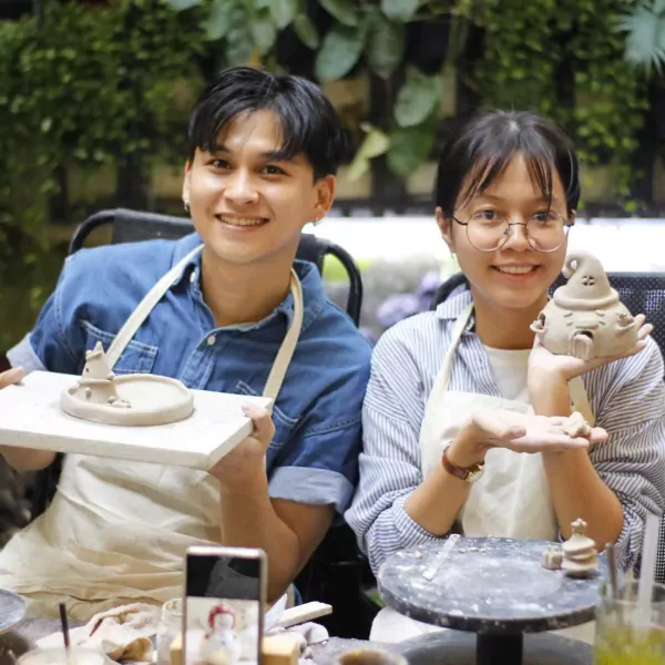Couple smiling and holding clay creations at a pottery workshop.