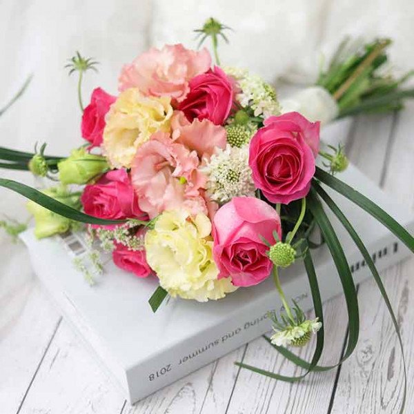 Bridal bouquet with pink roses, yellow lisianthus, and white accents on a book.