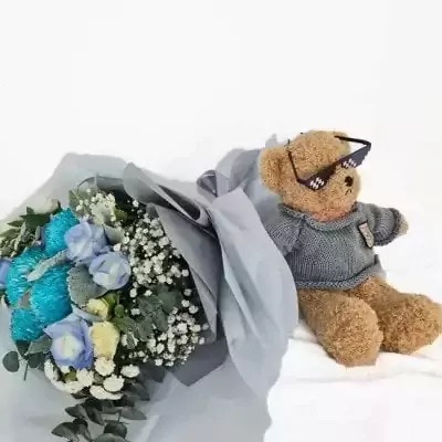 Teddy bear with sunglasses next to a bouquet of blue and white flowers.