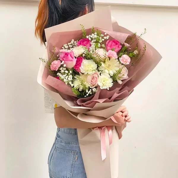 Bouquet of pink and white roses, chrysanthemums, carnations, and baby's breath in brown and pink paper wrap.