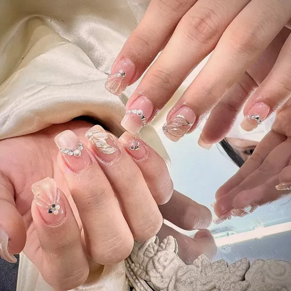 Nails adorned with rhinestones, pearls, and delicate floral embellishments.