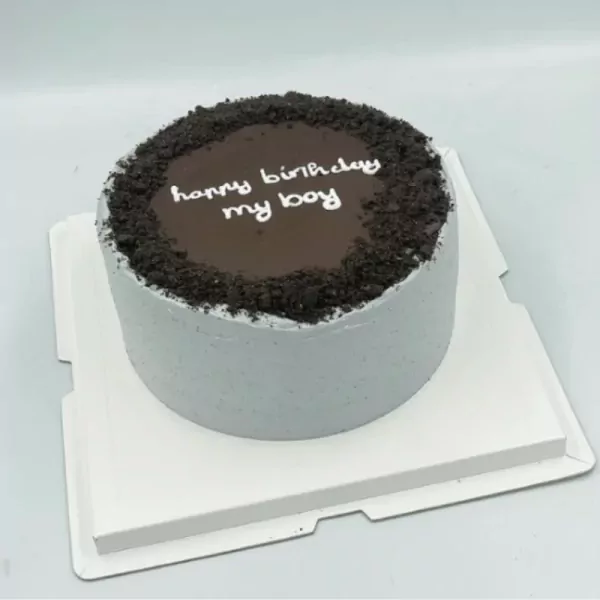 A round grey cake with chocolate ganache and cookie crumbs, reading "happy birthday my boy".