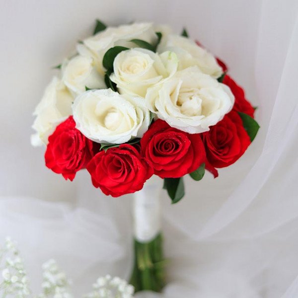 Bridal bouquet of red and white roses with a white ribbon stem, with tiny white flowers below.