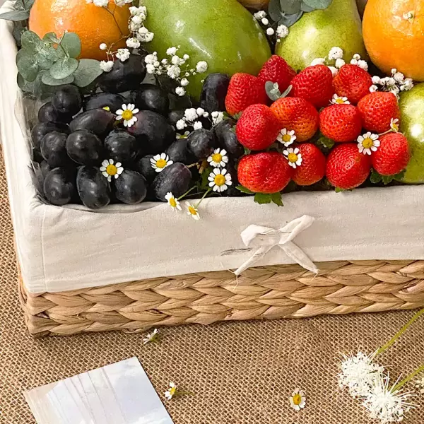 Fruit basket with strawberries, grapes, pears, oranges, and daisies.