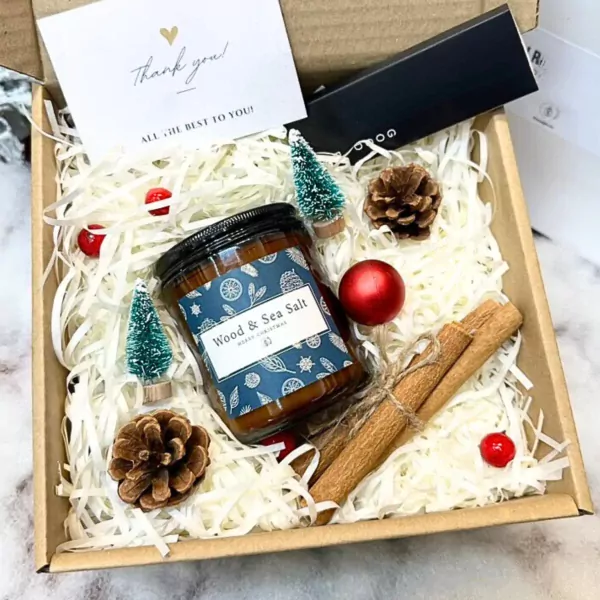 Christmas gift box with candle, pinecones, cinnamon sticks, mini trees, and ornaments.