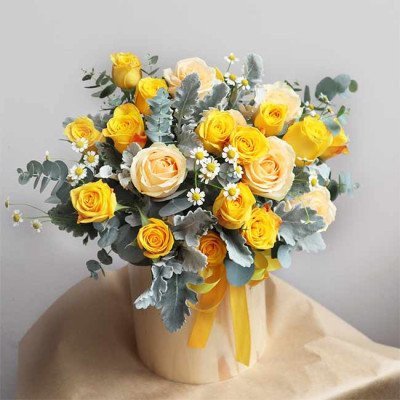 Box of yellow and cream roses with daisies and silver foliage.
