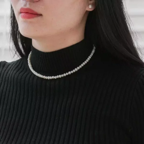 Close-up of a woman wearing a delicate pearl necklace and a black turtleneck.