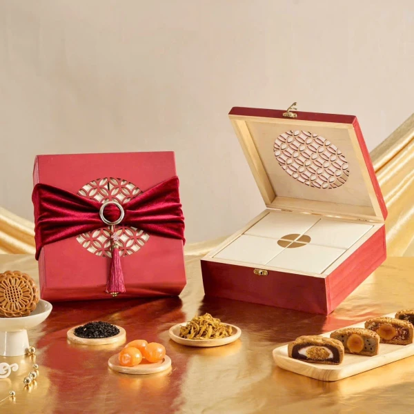 Red gift box with velvet ribbon and tassels, open wooden box with mooncakes and ingredients.