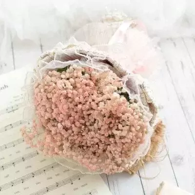 A bouquet of pink baby's breath flowers with lace and ribbon, resting on sheet music.