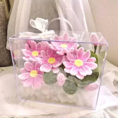 Pink lotus flowers in a clear square box with a white ribbon.
