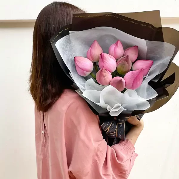 Woman in pink shirt holding a bouquet of pink lotus flowers wrapped in black and white paper.