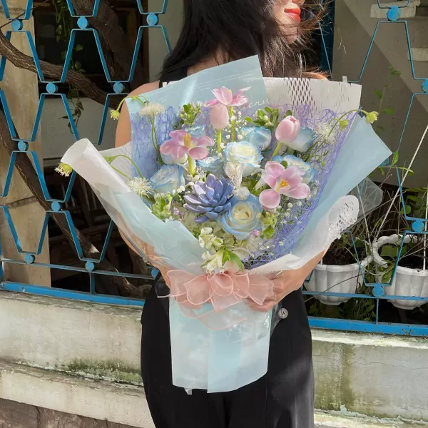 A woman holds a pastel blue and pink mixed flower bouquet.