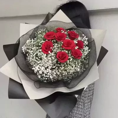 A bouquet of red roses and baby's breath flowers wrapped in black and white paper.