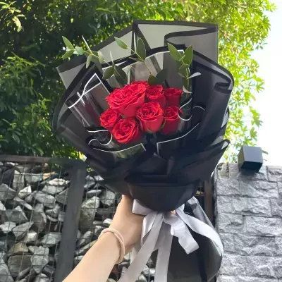 Hand holding a bouquet of red roses wrapped in black paper with a silver ribbon.