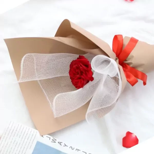 Red rose bouquet wrapped in brown paper and white tulle, tied with a red ribbon.