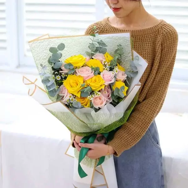 Woman in brown sweater holding a bouquet of yellow and pink roses with eucalyptus leaves.