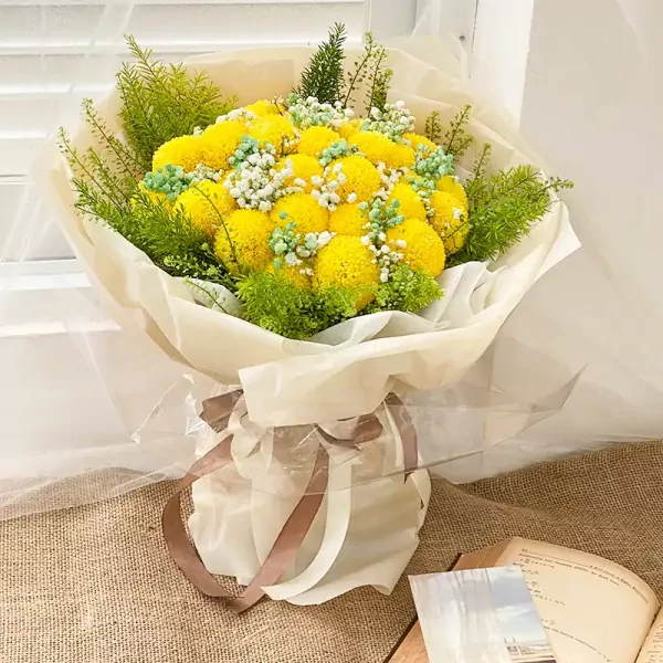 Yellow ping pong chrysanthemums with baby's breath and greenery in a cream and clear wrapper tied with ribbon.