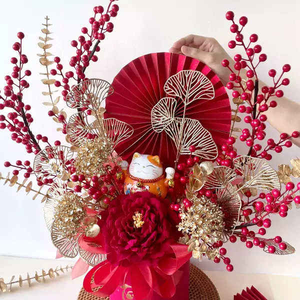 Maneki-neko cat with red fan, berries, and gold leaves in a red flower box.
